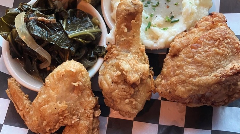 Three pieces of fried chicken with collard greens and mashed potatoes.