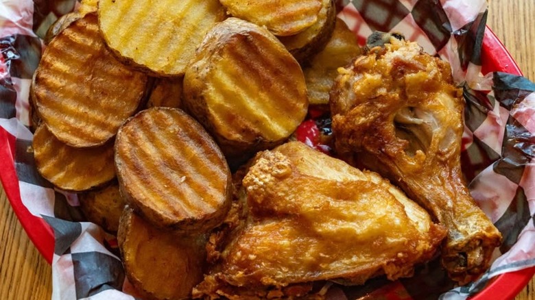 Pieces of fried chicken in red basket with thick-cut fries.