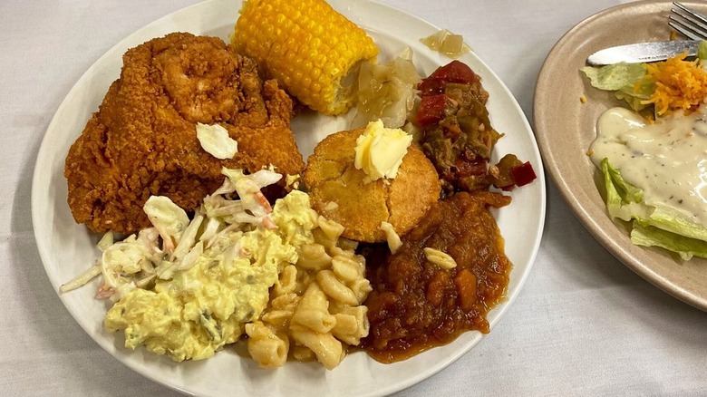 Fried chicken on plate with corn, cornbread, sides, and side salad.