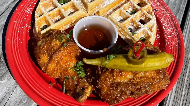 Pieces of fried chicken on red plate with sauce and waffles.