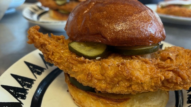Giant piece of fried chicken on bun with pickles.