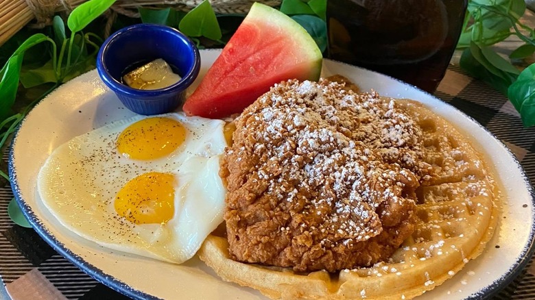 Fried chicken on plate with waffles, eggs, and watermelon slice.