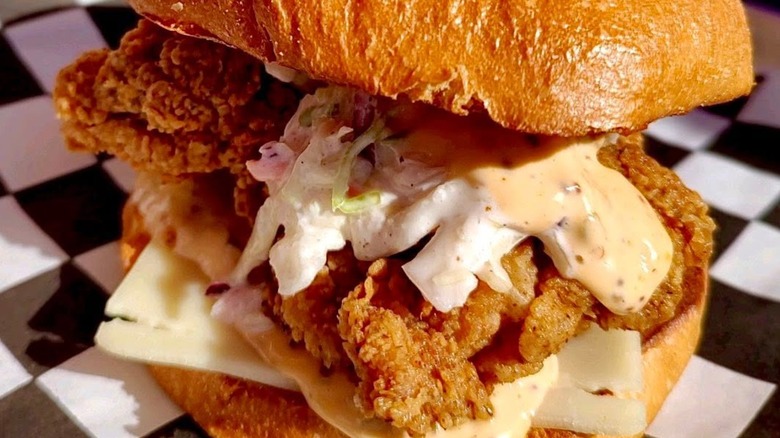 Fried chicken sandwich close-up with cheese, slaw, and sauce.