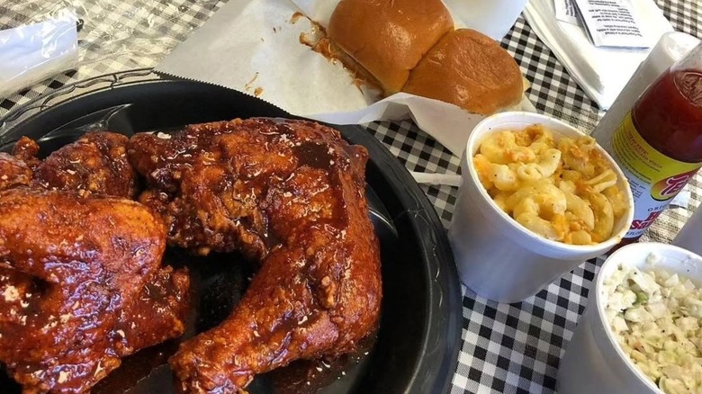 Saucy fried chicken with sides and rolls on table.