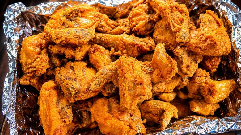 Tray covered with aluminum foil and assorted pieces of fried chicken.