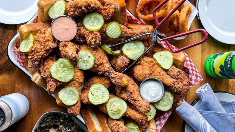 Platter of fried chicken with pickles, sauces, and bread.