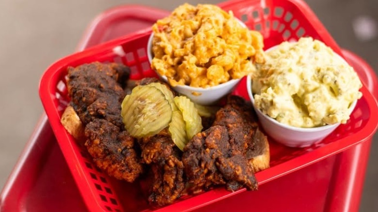 Extra spicy-looking fried chicken in red tray with sides and pickles.