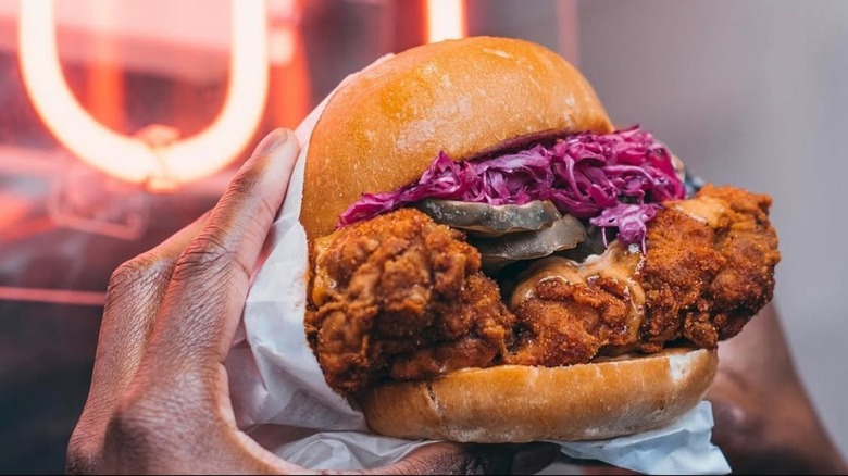 Hands holding fried chicken sandwich with pickles and slaw.