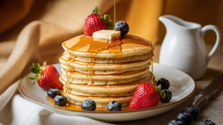 A plate of pancakes with fruit, butter, and syrup