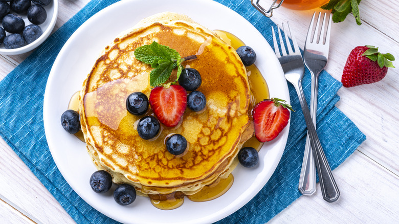 A plate of pancakes with fruit and syrup on a table