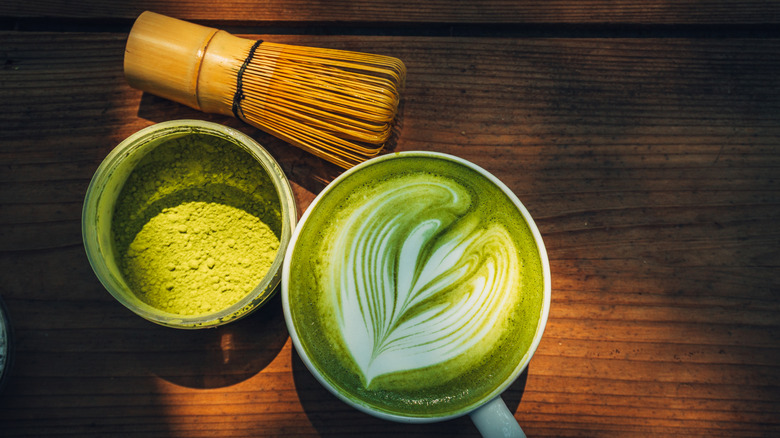 Matcha latte next to matcha powder with a bamboo whisk on a wooden background