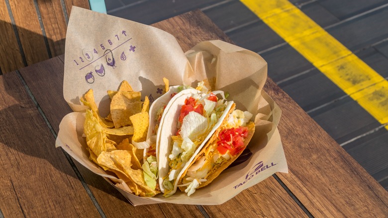A Taco Bell meal with chips, soft tacos, and hard shell tacos sits outside on a wooden table