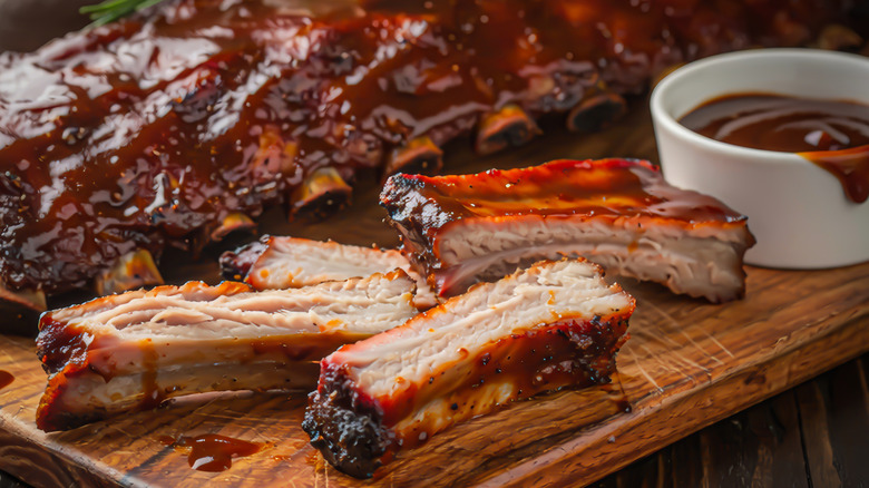 Baby back pork ribs next to a whole cooked rib rack and a ceramic ramekin of barbecue sauce