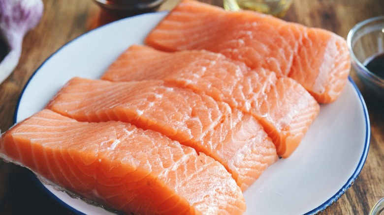 Filets of raw salmon surrounded by seasonings and marinades