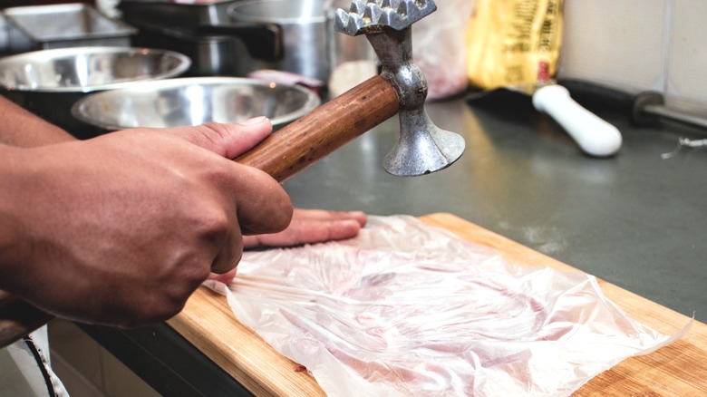 A cook using a meat mallet on a piece of raw chicken