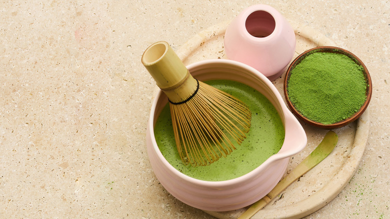 Matcha being made in a ceremonial bowl, along with matcha powder in a bowl.