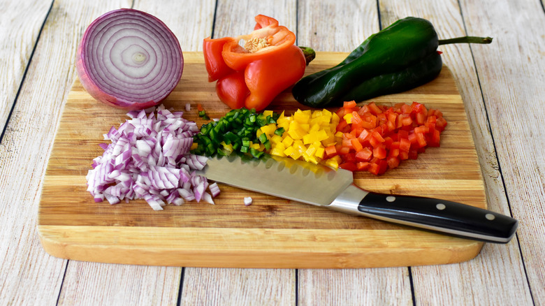 chopped red onion, bell peppers with knife on a wooden cutting board