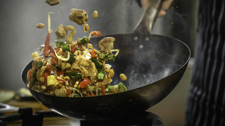 Wok cooking in action, with ingredients being tossed and smoke rising from the wok.