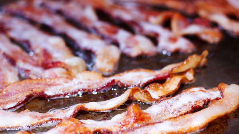 Strips of bacon frying on a flattop