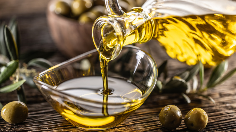 Glass bottle pouring oil into a small glass bowl
