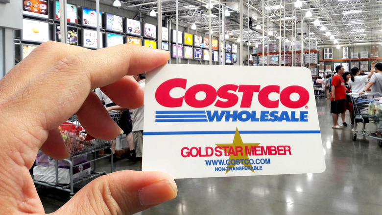 A person holds up their Costco membership card inside of a Costco warehouse