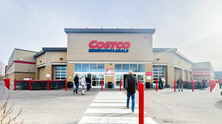 The exterior of a Costco wholesale in daylight, with many people walking up to it