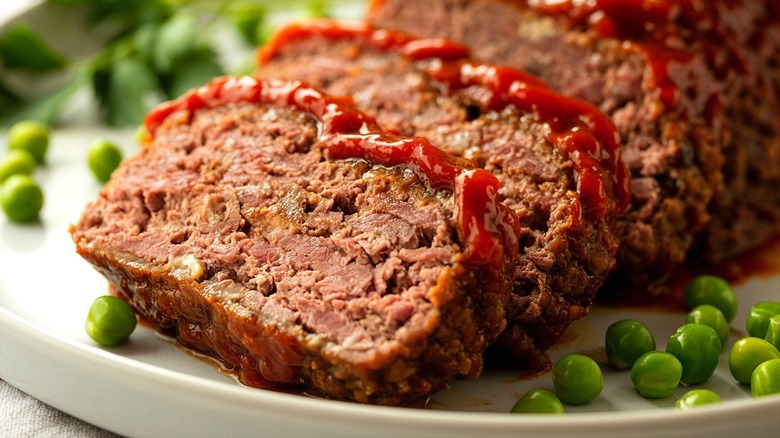 Slices of meatloaf with tomato sauce and green peas on a white plate