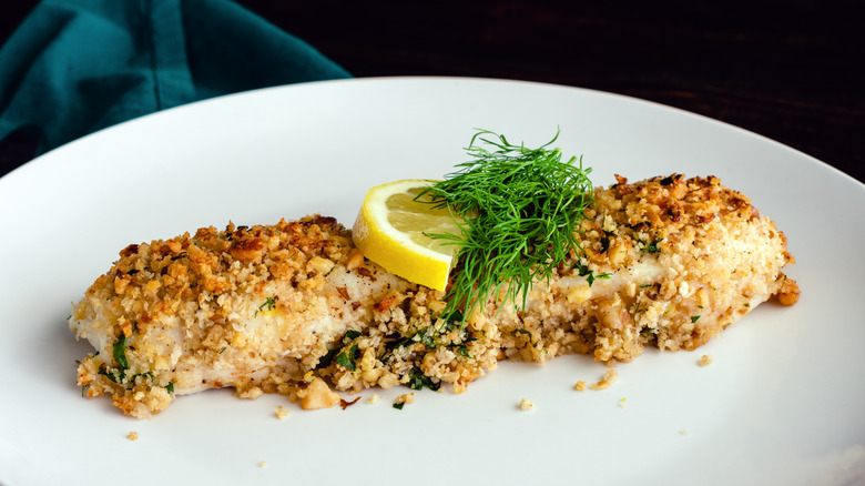 breaded white fish fillet on plate with lemon and dill