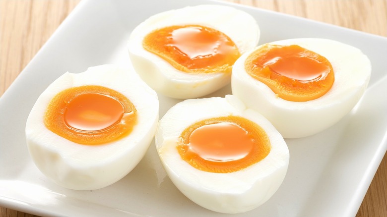 Four halved soft-boild eggs on a square white plate