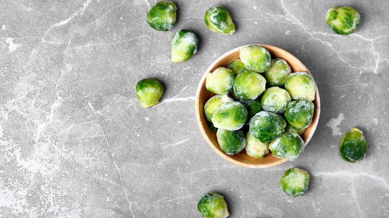 Frozen Brussels sprouts in a bowl and on a gray stone background.