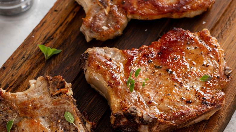 Three beautifully caramelized pork chops on a cutting board, topped with herb sprigs.