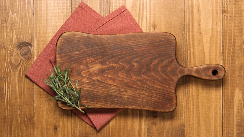 A wooden cutting board on a cloth napkin with fresh rosemary