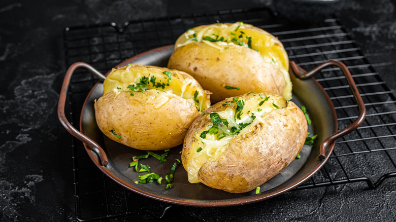 Three baked potatoes with herbs in a shallow round pan on cooling rack.