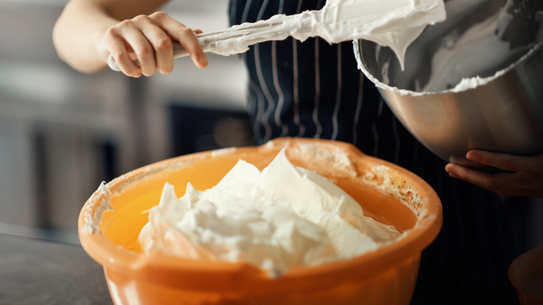 caucasian woman's hand over two mixing bowls of frosting