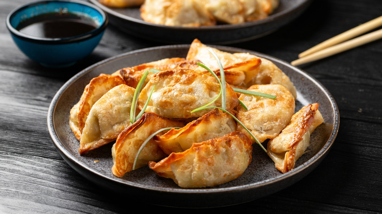Crispy fried dumplings on a plate with garnish and chopsticks and a bowl of sauce in the background