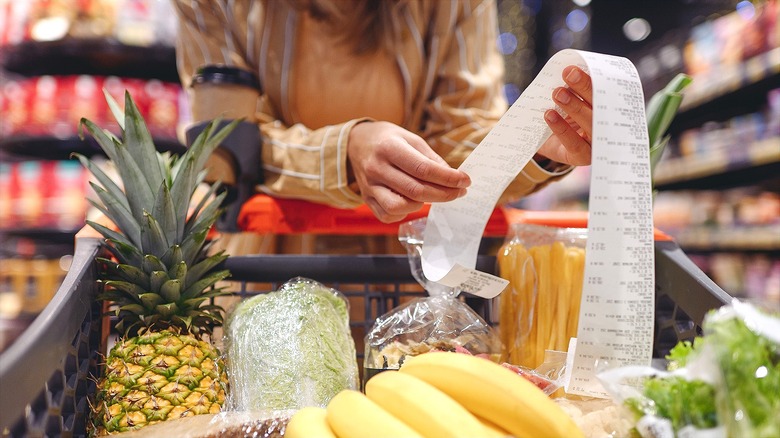 Woman holding a long receipt above a grocery cart full of food