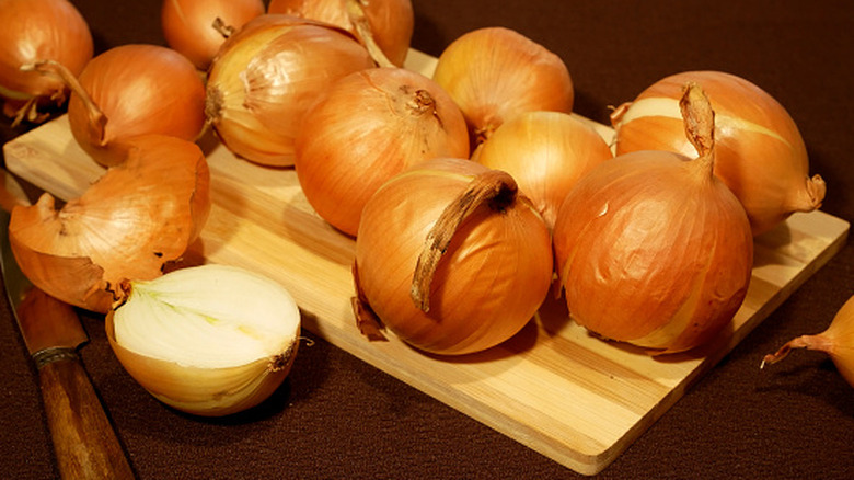 Onions on a wooden cutting board with a knife on the table, one onion cut in half.