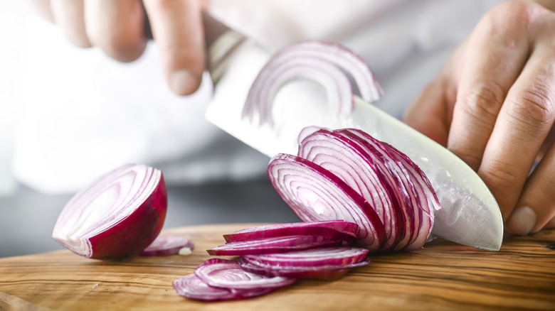 Man hands cutting red fresh onion with knife.
