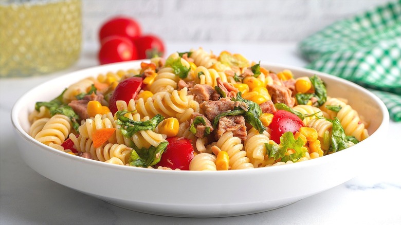 Fresh pasta salad with tuna, halved cherry tomatoes, corn, and chopped greens in a shallow white bowl.