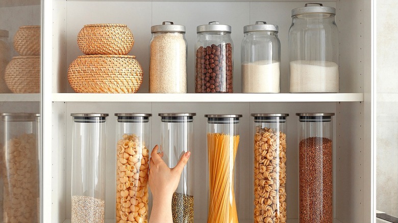 Hand grabbing a container of dried lentils from an exposed shelf full of dry goods in glass jars