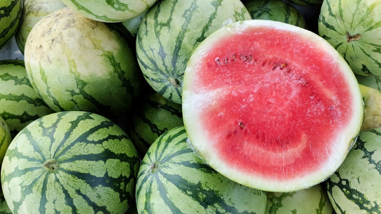 Half of a watermelon laying on many full watermelons