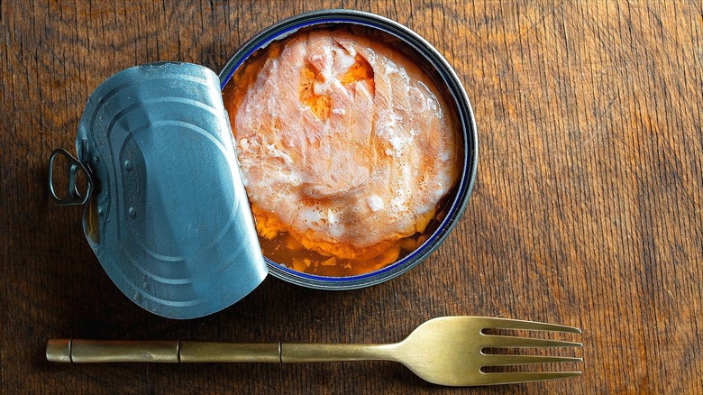 Opened can of salmon next to a metal fork on a wooden surface