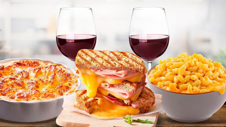 A glass of red wine next to a grilled cheese sandwich, baked mac and cheese and potatoes au gratin.