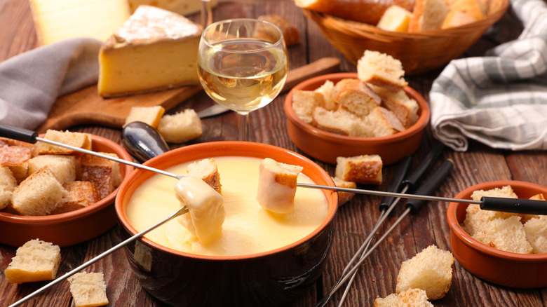 A glass of white wine beside a pot of cheese fondue.