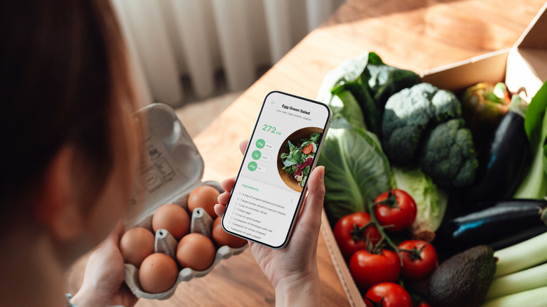 A person looking at a smartphone over bags of groceries.