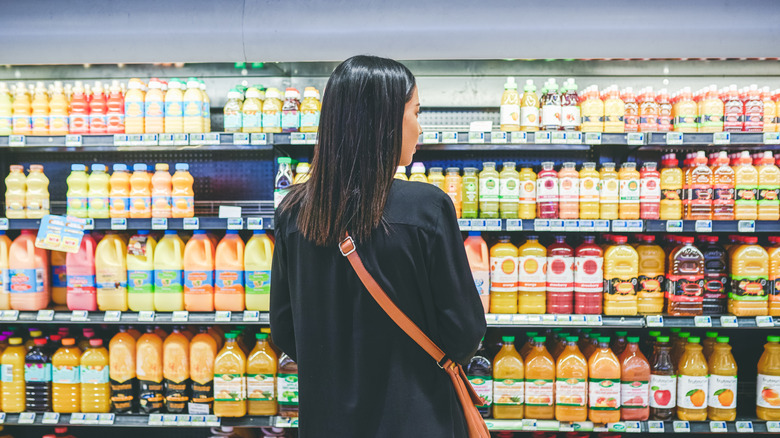 A woman facing the refrigerated beverages section in a grocery store.