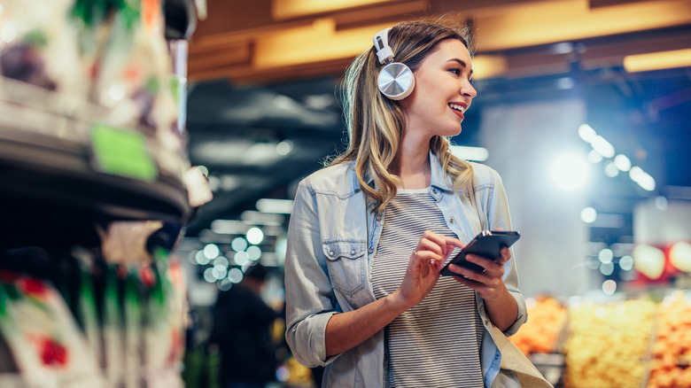 A woman shopping in a supermarket while wearing headphones.