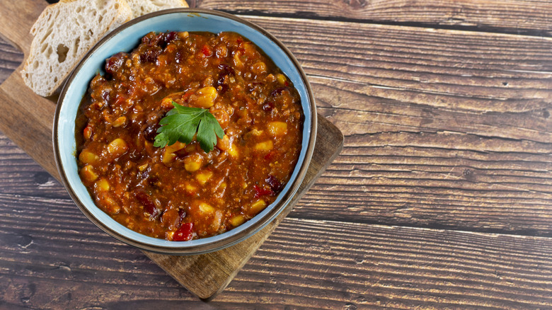Bowl of chili on a wooden board with a slice of bread