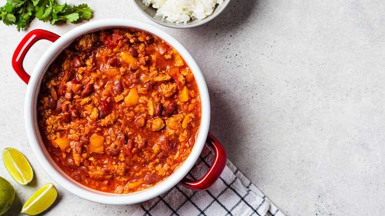 Bowl of chili with lemon wedges, cilantro, and a table cloth on the side