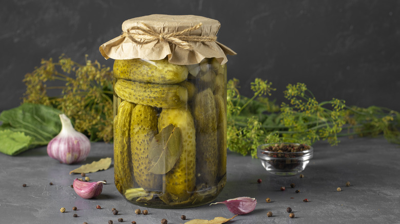 Homemade pickled cucumbers with garlic, horseradish, pepper and dill in glass jar on gray background